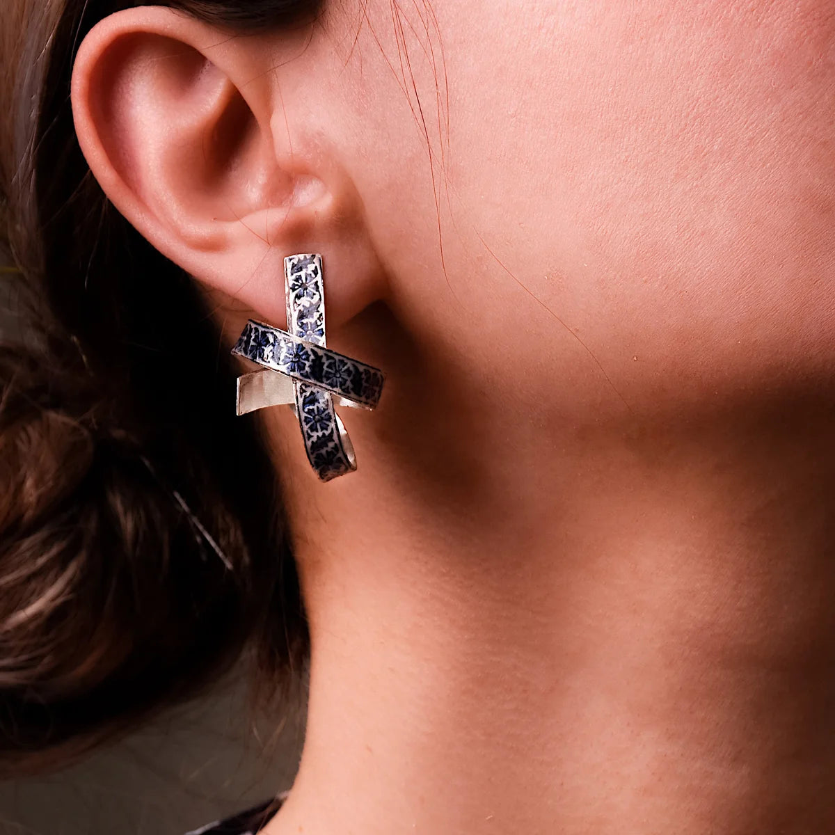 woman wearing unusual handmade silver earrings with blue black floral patterns