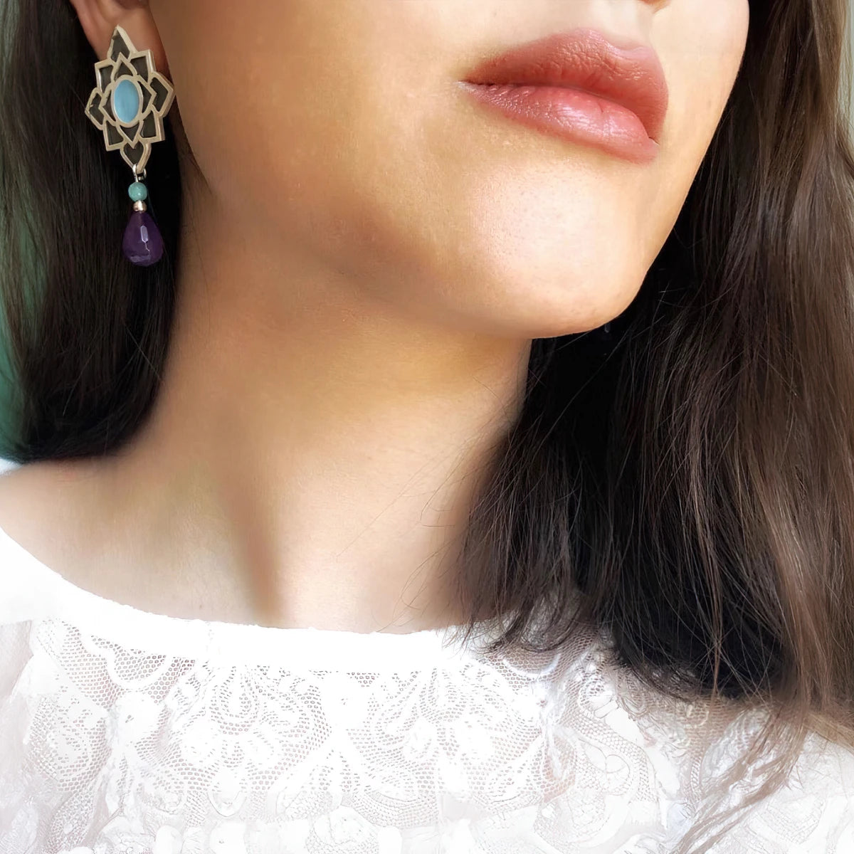 model wearing Handmade sterling silver lotus dangle earrings with oxidized silver petals, blue and violet enamel centers, aqua accent beads, and faceted purple crystal teardrops.