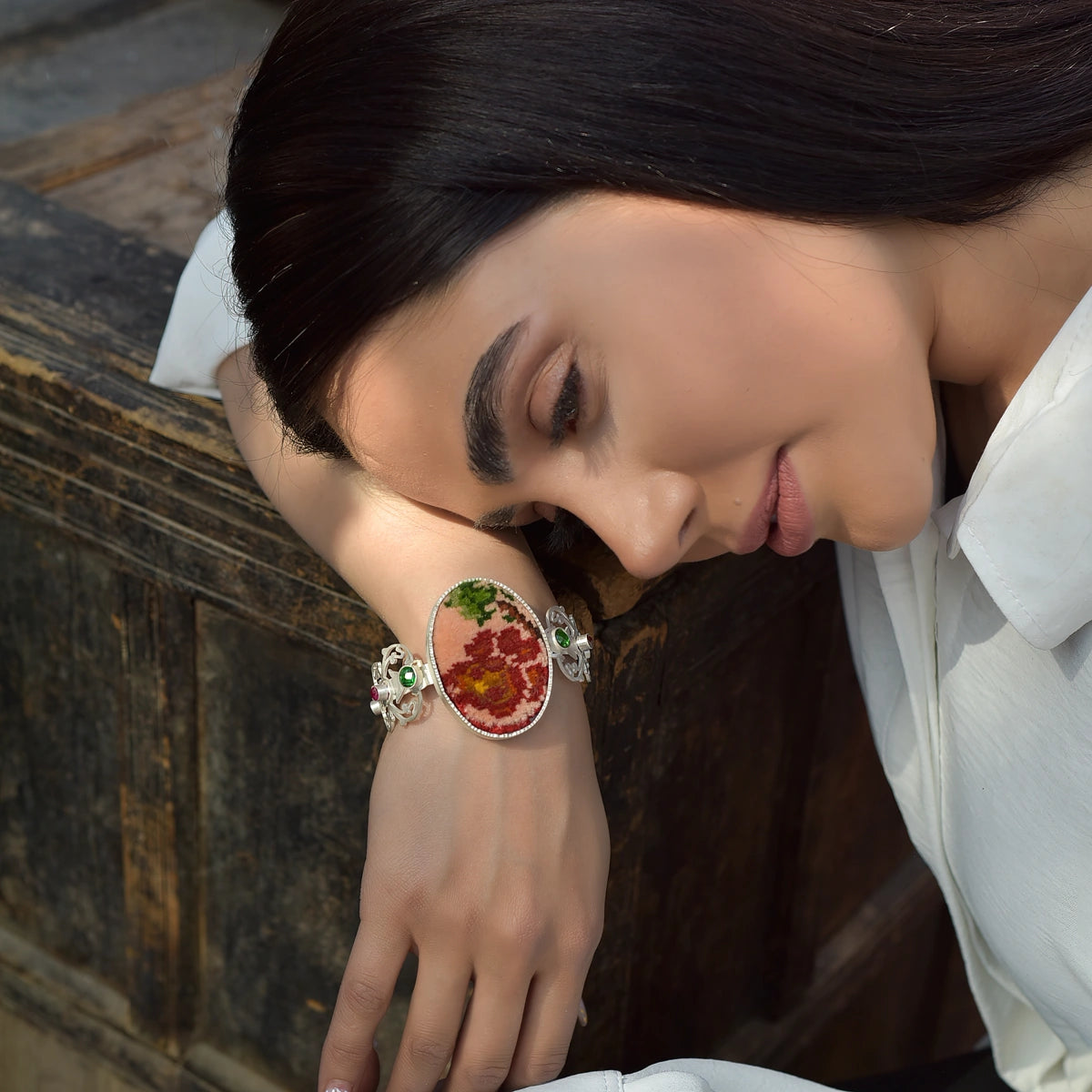 model wearing handmade intricate openwork silver statement bracelet with oval Persian style rug and green and pink crystals