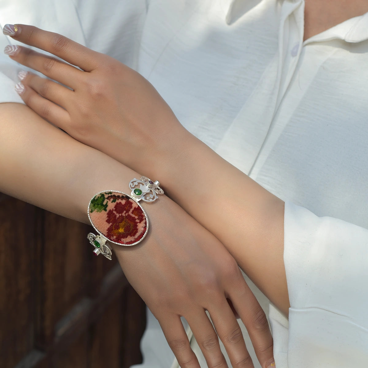 model wearing handmade intricate openwork silver statement bracelet with oval Persian style rug and green and pink crystals