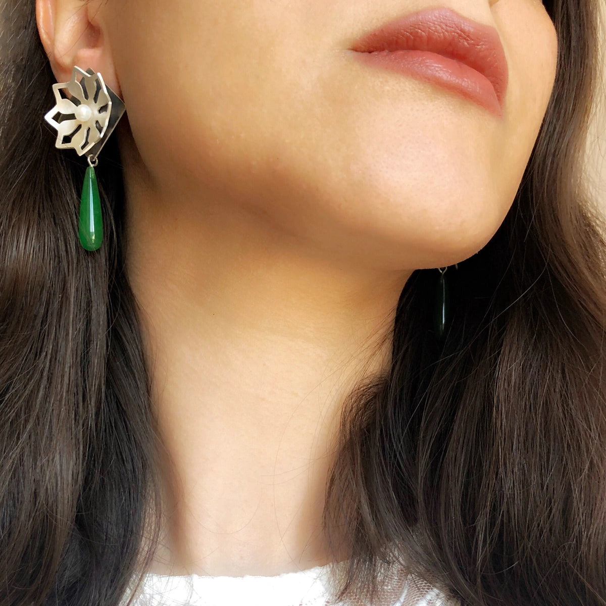 model wearing Pair of earrings with silver star design and green teardrop crystals and pearl