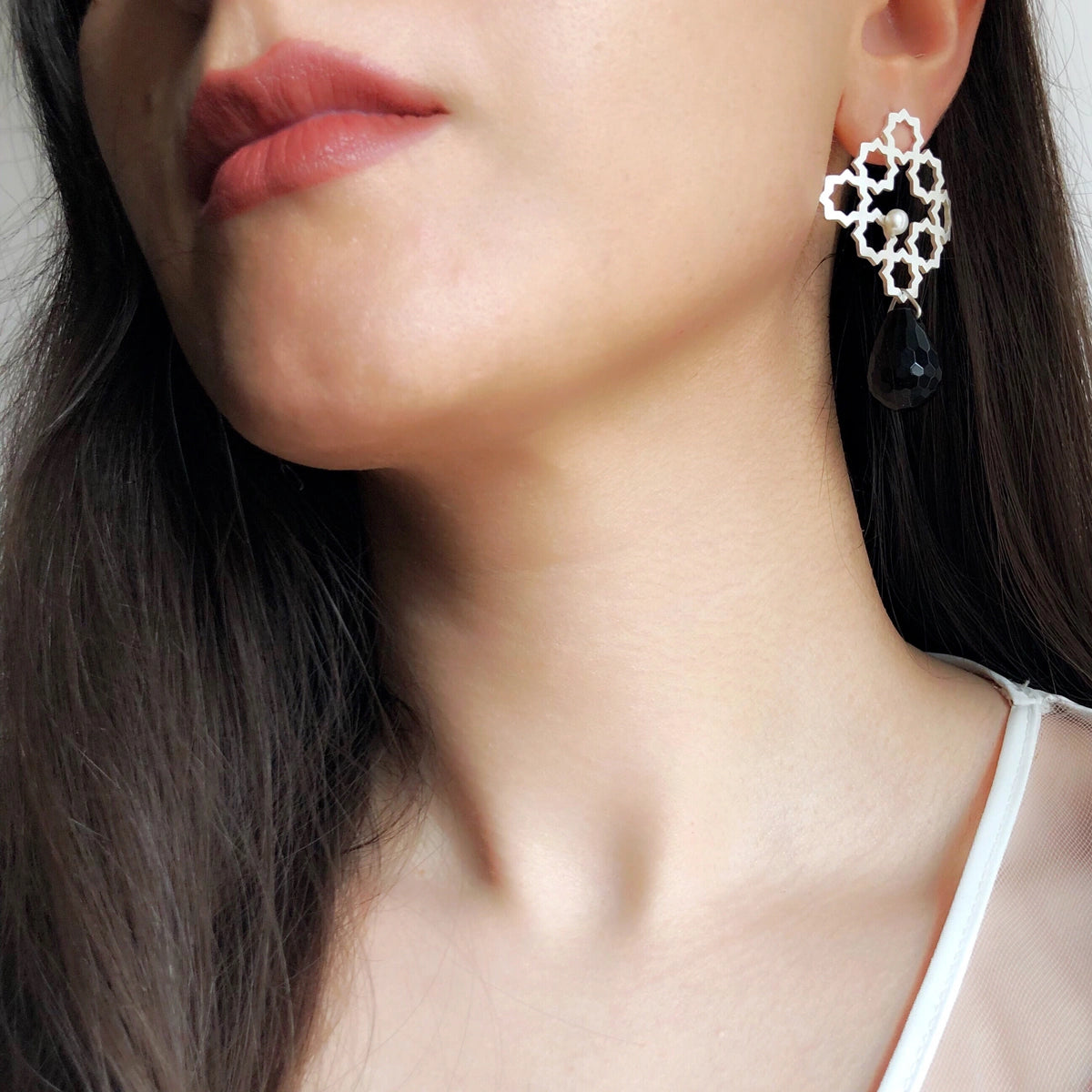 model wearing Pair of earrings with geometric lace design and small pearl and black teardrop onyx pendants