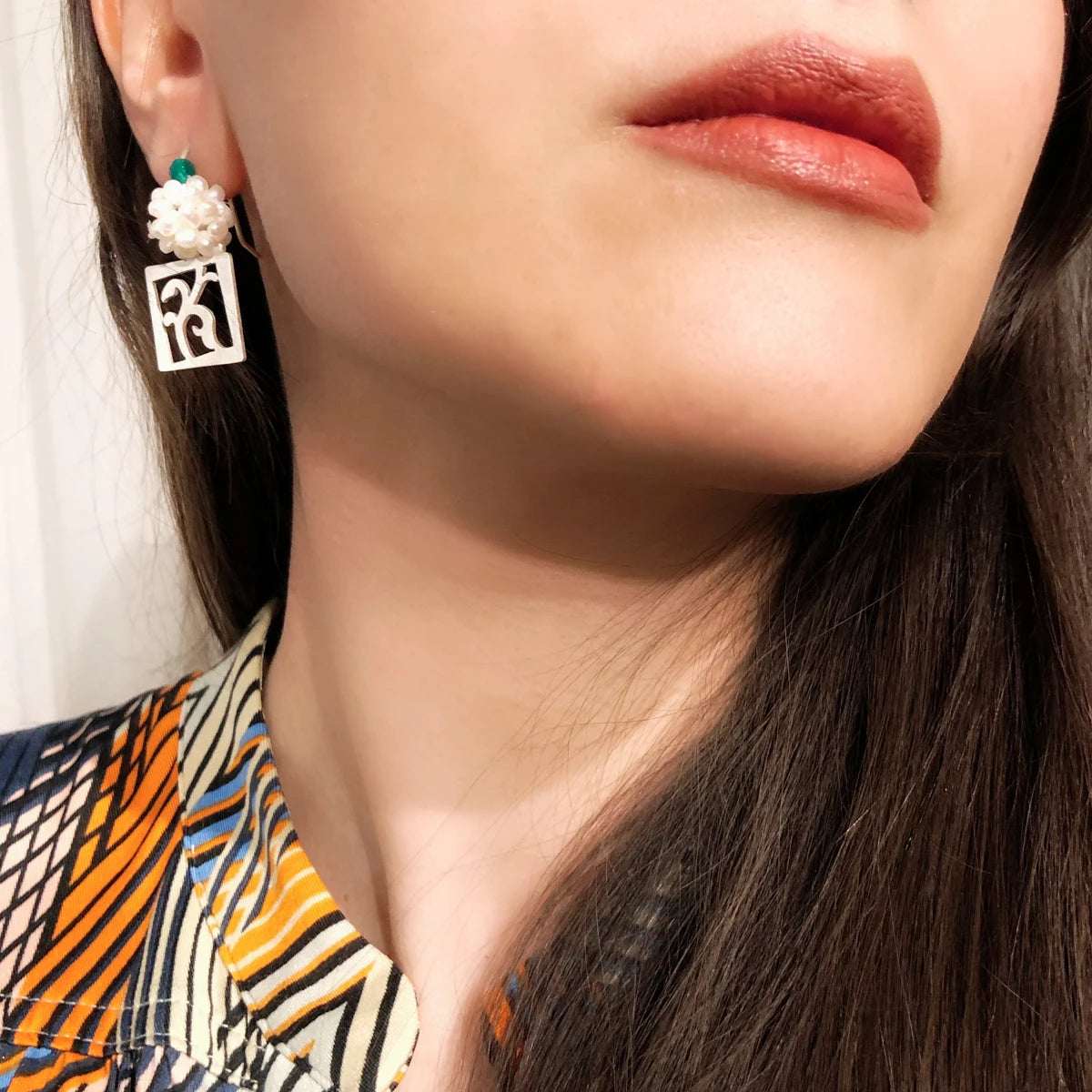 model wearing handmade openwork silver floral square drop earrings decorated with a cluster of cultured pearls and green agate