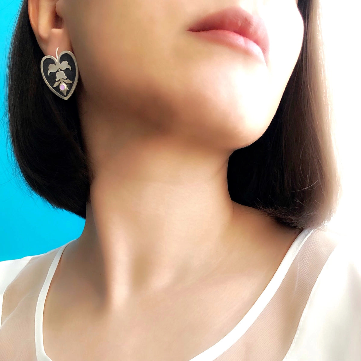 model wearing handmade heart-shaped silver earrings with motif and cubic zirconia