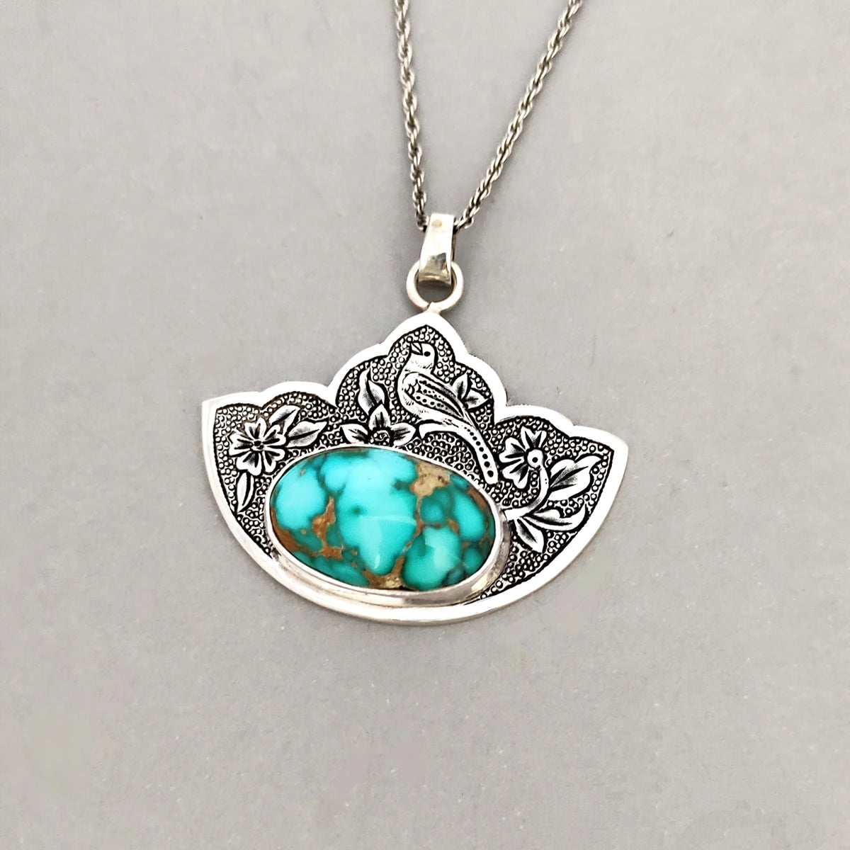 intricately hand-engraved pendant necklace with bird and glower motifs decorated with oval Persian Turquoise