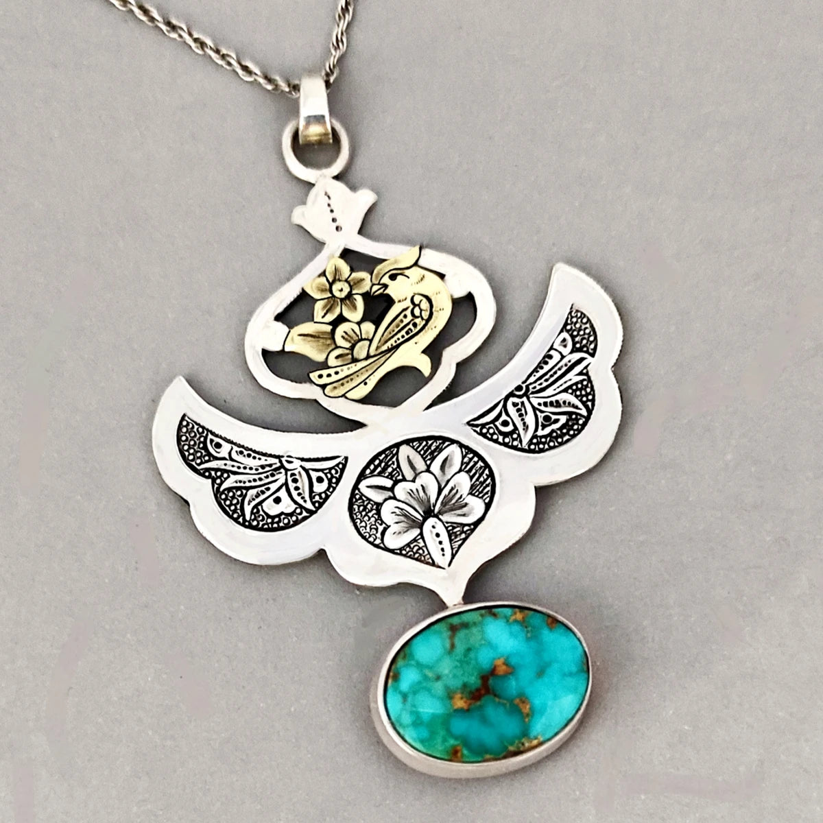 Hand-engraved silver pendant with floral and bird motifs decorated with a turquoise