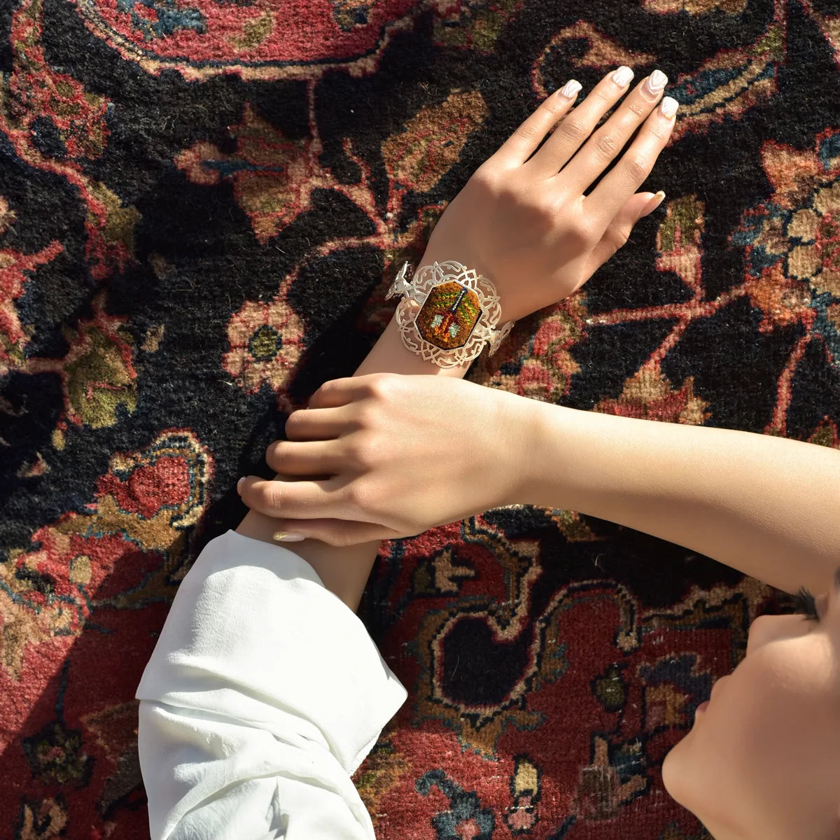 model wearing handmade silver bracelet with intricate openwork and Silk handwoven Persian rug