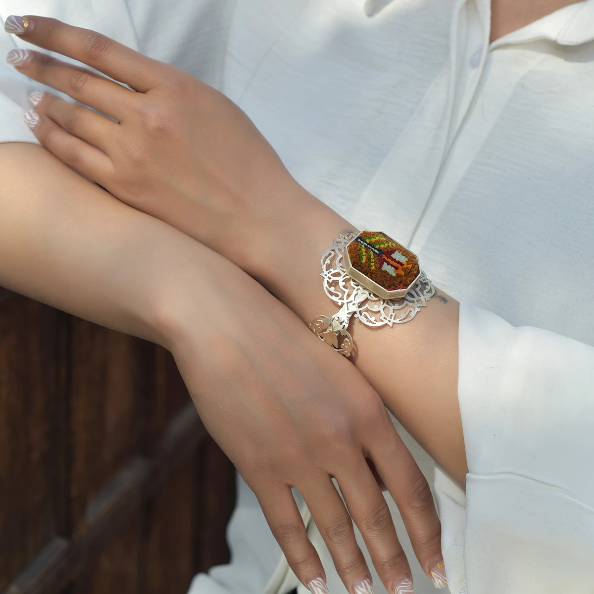 model wearing handmade silver bracelet with intricate openwork and Silk handwoven Persian rug
