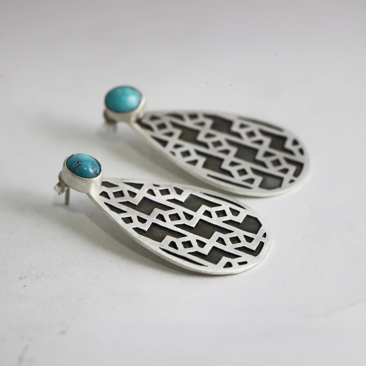 handmade silver teardrop earrings with oxidized parts and geometric patterns decorated with turquoise