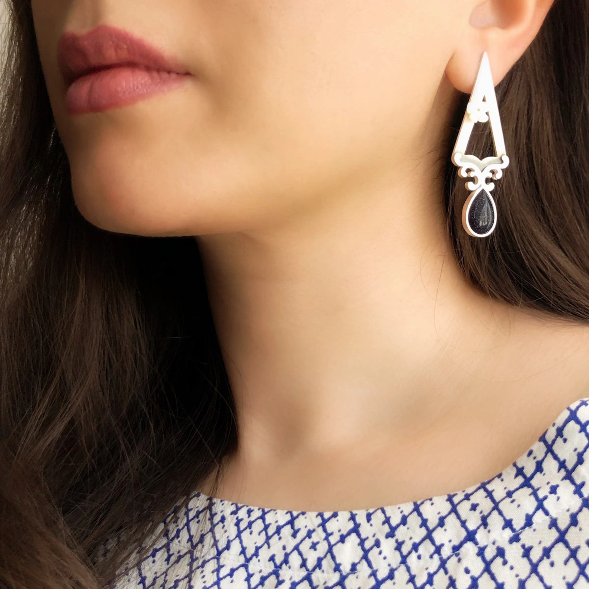 model wearing triangular earrings decorated with floral motifs, mother of pearl flower and blue star gemstone.