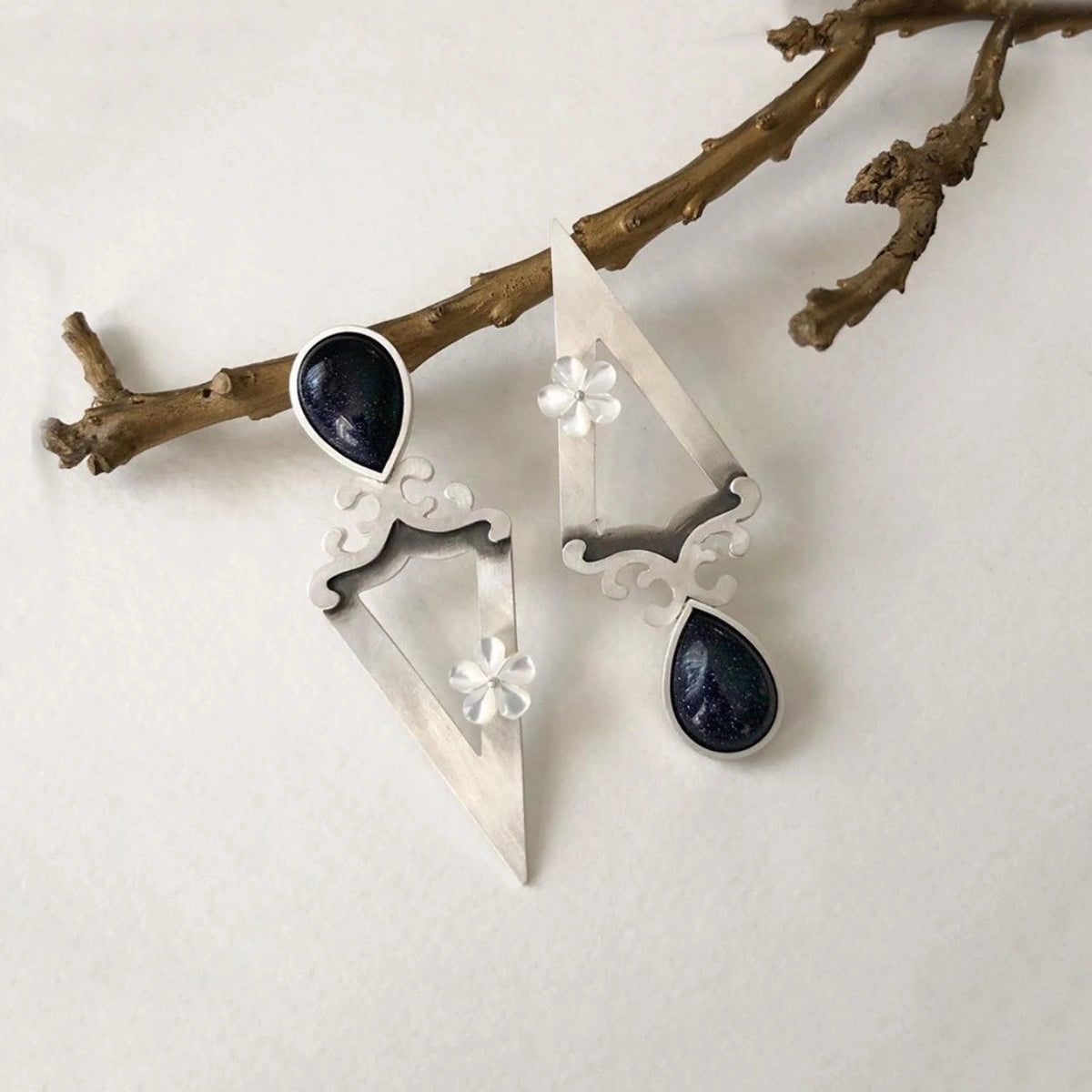 triangular earrings decorated with floral motifs, mother of pearl flower and blue star gemstone.