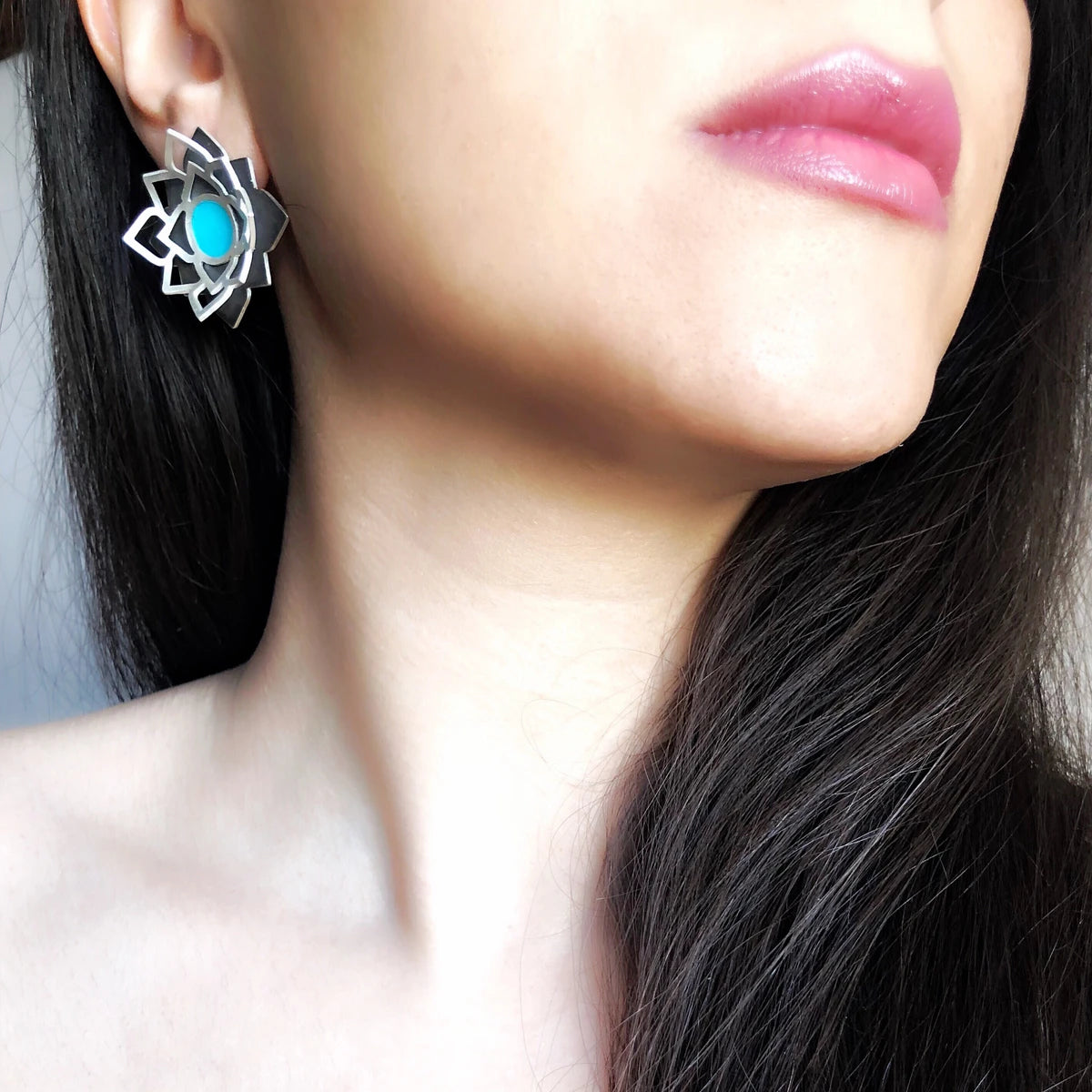model wearing handmade sterling silver lotus stud earrings with layered openwork design, oxidized silver base, and turquoise-blue enamel centerpiece.