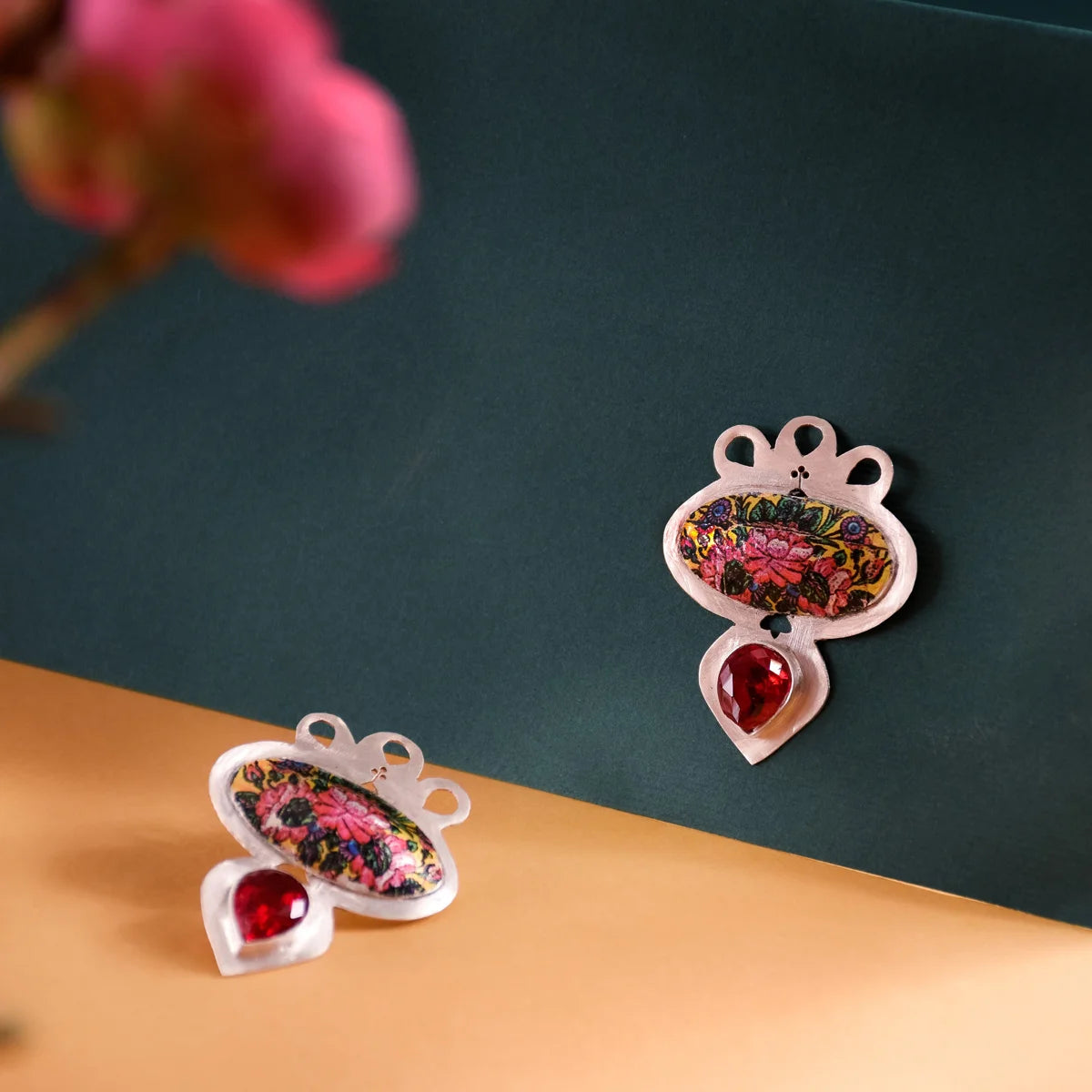 Handmade silver statement stud earrings in oval shape, decorated with hand-printed floral patterns and tear-drop red cubic zirconia crystals. 