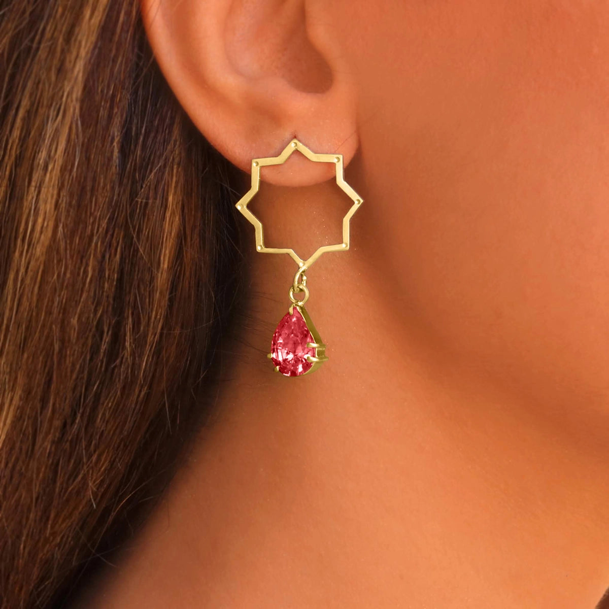 model wearing handmade gold plated silver star shaped drop earrings with red crystals