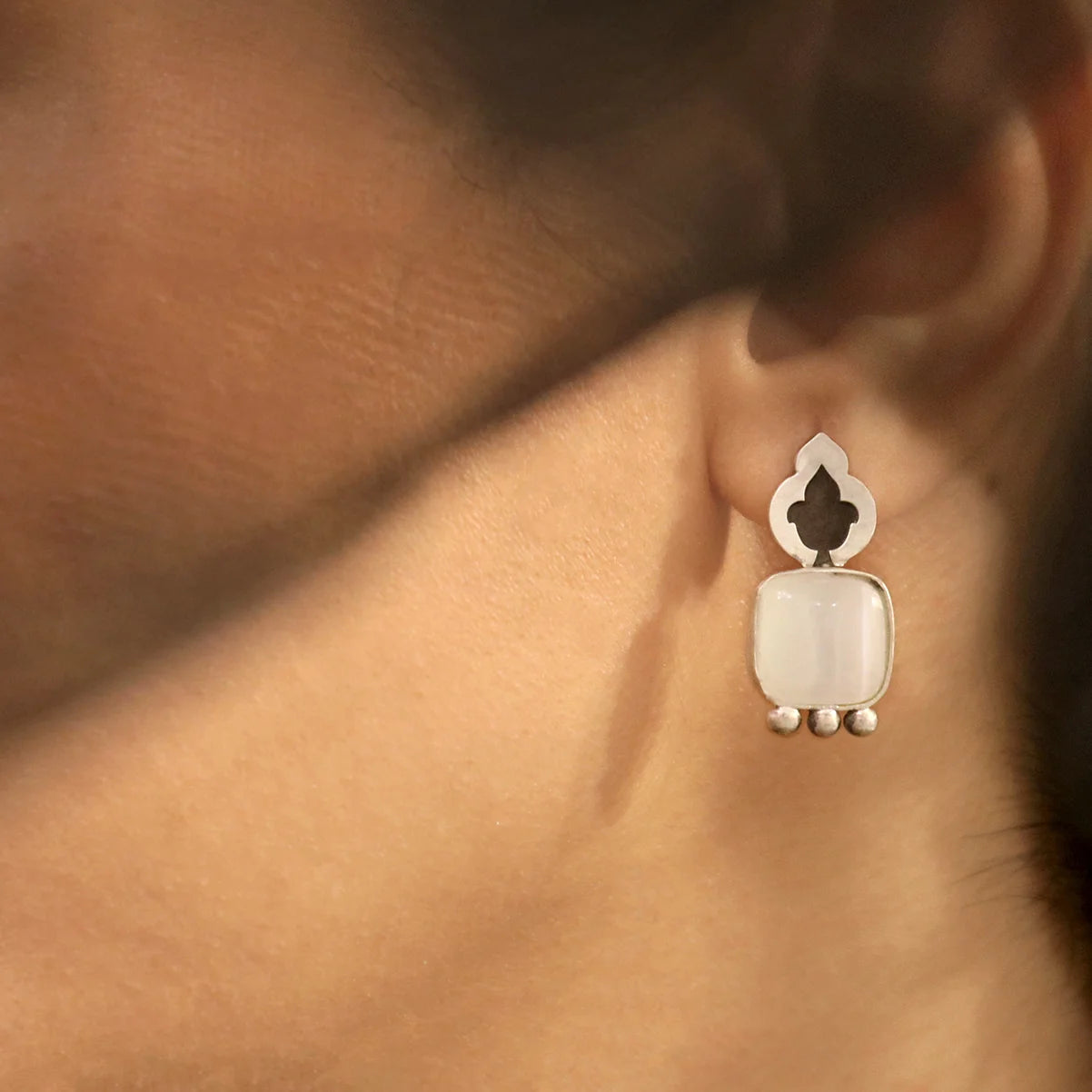 model wearing handmade silver stud earrings decorated with cat's eye gemstones