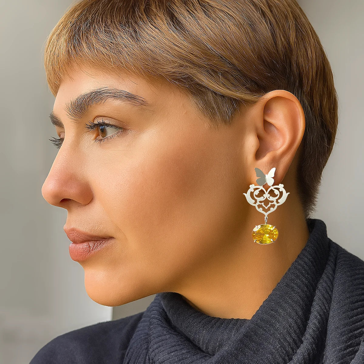 model wearing convertible sterling silver earrings with butterfly studs and detachable floral openwork panels featuring oval yellow crystal drops; two-way asymmetrical design