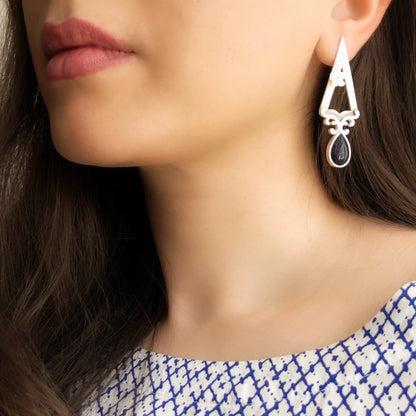 model wearing triangular earrings decorated with floral motifs, mother of pearl flower and blue star gemstone. 