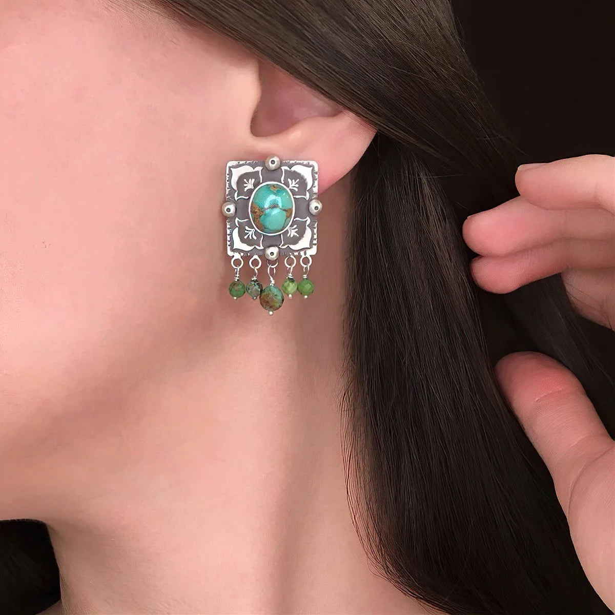 model wearing handcrafted oxidized silver stud earrings decorated with turquoise gemstones and floral motifs.